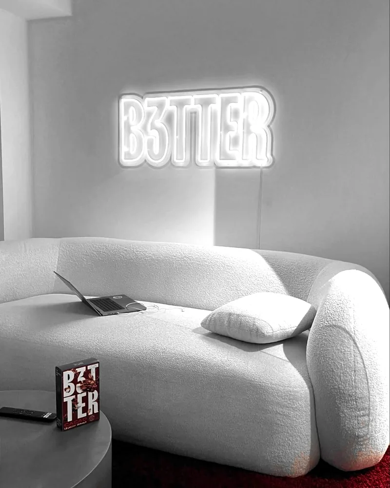 Plató del B3TTER Podcast: el letrero de neón B3TTER sobre un sofá blanco; al bajar se encienden las luces de color, con una caja roja de granola B3TTER en la mesa.
