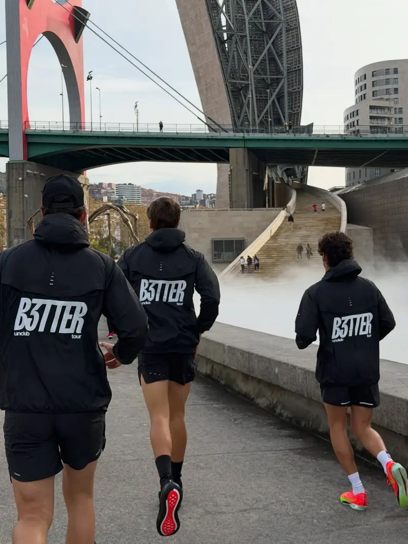 Tres del club de carrera, con sudaderas de B3TTER, corren bajo un puente.
